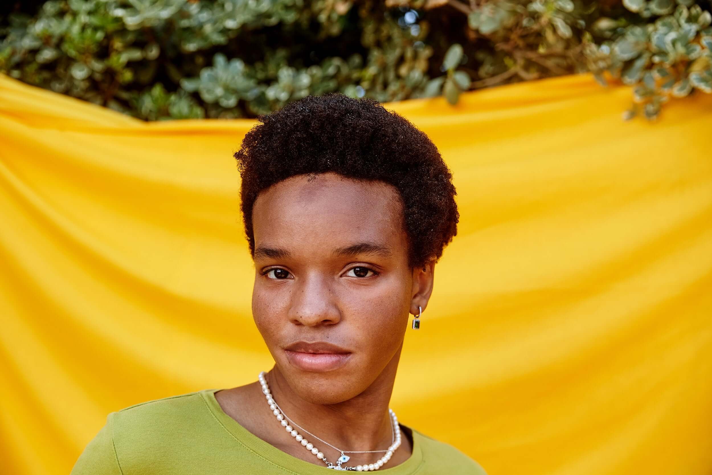 Close-up of an LGBTQ young person in a green shirt, standing in front of a yellow backdrop